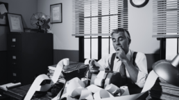 A 1950s man at a desk with paper everywhere looking perplexed