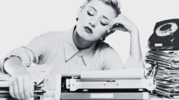 A 1950s woman at a desk full of papers looking sad