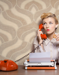 A 1950s woman at a desk, with a typewriter on a red phone, trying to figure out conversion copy.