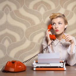 A 1950s woman at a desk, with a typewriter on a red phone, trying to figure out conversion copy.